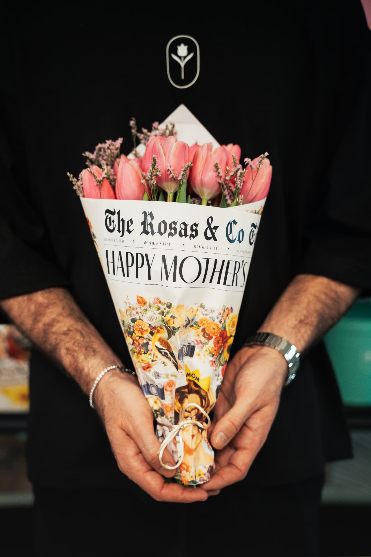Hands holding a Rosas & Co. newspaper-wrapped tulip bouquet